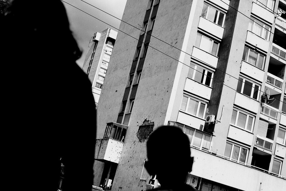 Boy looking at a bombshelled house in Sarajevo.