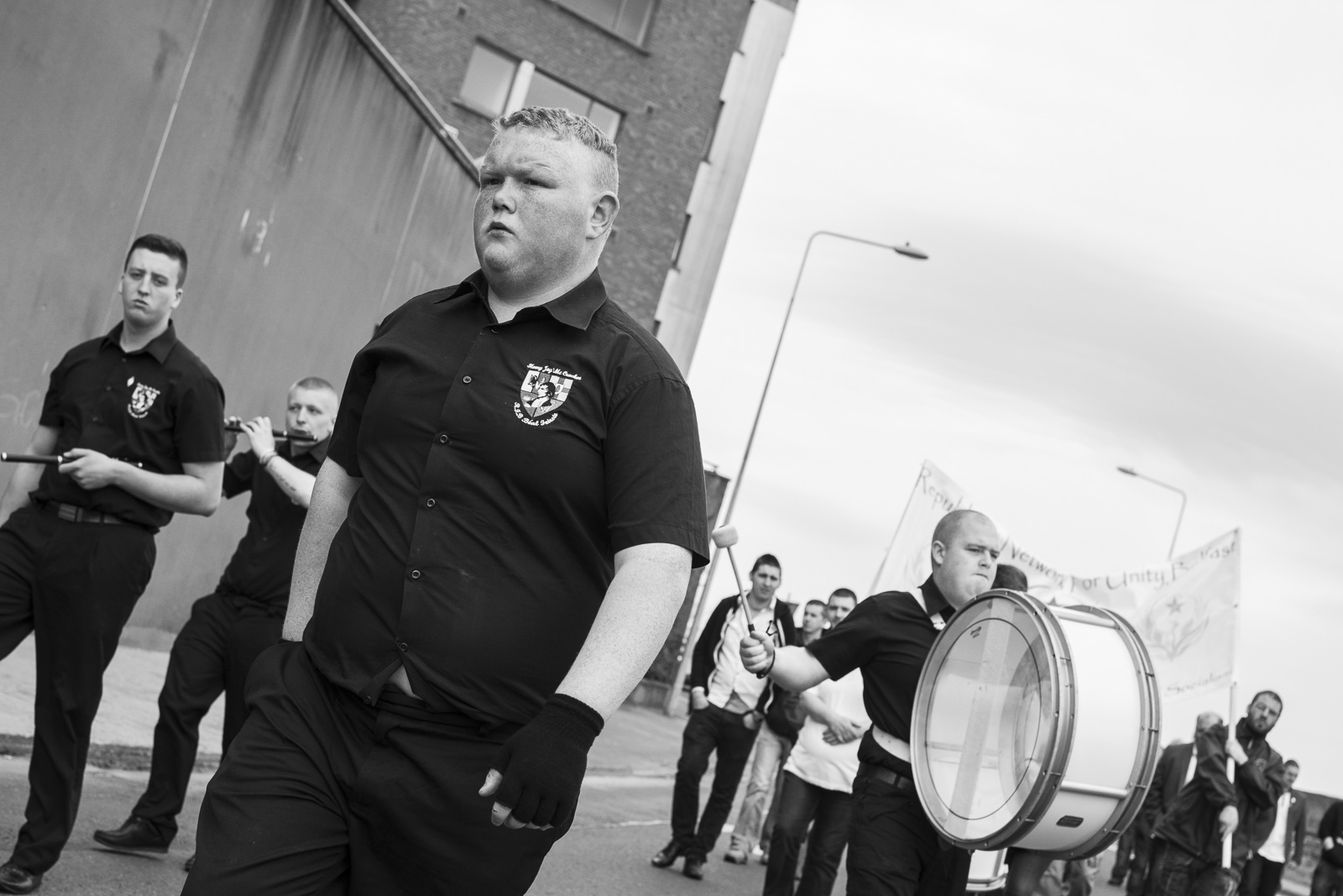 Young members of the Henry Joy McCracken Republican Flute Band marching in uniform with flutes and a bass drum on a street during a parade